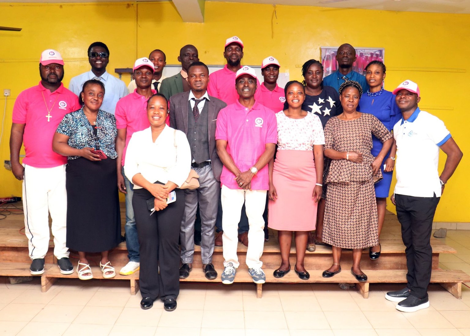 A group of WEWAD volunteers and partners, many in branded pink polo shirts and caps, standing together after a programme session in Nigeria.